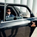 Leeds Chauffeur Service by MCR EXEC with a black 2025 Mercedes E-Class in Leeds city centre, chauffeur opening the door for a business traveller, MCR-EXEC plate visible.