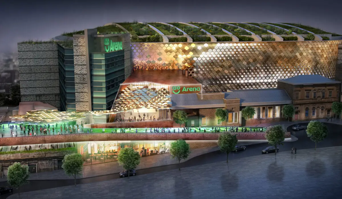 Night view of Co-op Live Arena in Manchester, with illuminated golden exterior and rooftop greenery. Crowds are visible entering the venue, representing luxury event chauffeur services by MCR EXEC.