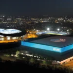 Aerial night view of Manchester’s Co-op Live Arena and Etihad Stadium illuminated against the city skyline, showcasing the venues for concerts and events served by MCR EXEC Chauffeur Services.