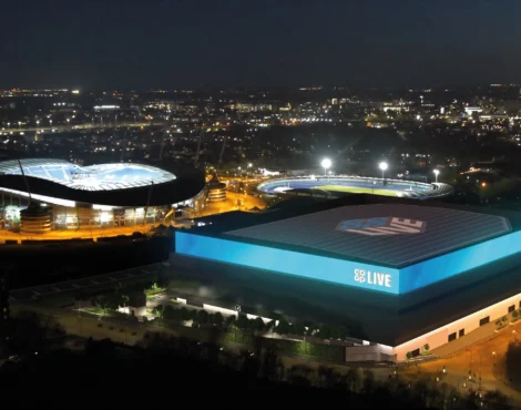 Aerial night view of Manchester’s Co-op Live Arena and Etihad Stadium illuminated against the city skyline, showcasing the venues for concerts and events served by MCR EXEC Chauffeur Services.