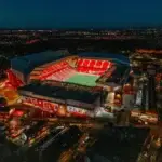 Aerial night view of Anfield Stadium in Liverpool illuminated during an evening match, representing MCR EXEC’s luxury chauffeur services for Liverpool FC fans and VIP guests.