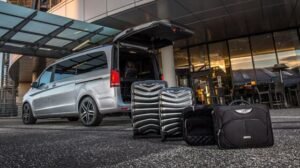 Luxury silver Mercedes V-Class parked outside a modern terminal building with luggage neatly arranged beside the vehicle. Represents MCR EXEC’s airport chauffeur services.