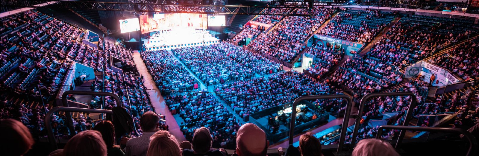 Panoramic interior view of a packed Motorpoint Arena during a live event, with stage lights illuminating a large audience seated across multiple tiers. Represents MCR EXEC’s Motorpoint Arena Chauffeur Services.