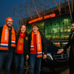 Three Dutch Manchester United supporters in orange scarves exiting a Mercedes MPV at Old Trafford, welcomed by a chauffeur with the MCR EXEC logo visible.