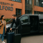 A black MPV parked outside the University of Salford with an international student and driver unloading suitcases