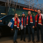 Three Finnish Manchester United fans stepping out of a luxury MPV outside Old Trafford with a chauffeur holding the door and the stadium in the backdrop.