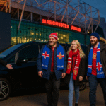 Three Icelandic Manchester United fans in scarves and winter coats stepping out of a luxury MPV outside Old Trafford, greeted by a suited chauffeur.