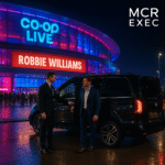 A professional MCR EXEC chauffeur assists a client outside a luxury Mercedes V-Class at Co-op Live arena on 10th June 2025, just before the Robbie Williams concert in Manchester.