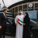 Chauffeur opening luxury car door for Emirati tourists holding UAE flag outside Etihad Stadium