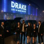 A group of five stylish friends arrive at night for a Drake concert at a Manchester venue, stepping out of a black Mercedes V-Class as an MCR EXEC chauffeur welcomes them; Range Rover and S-Class vehicles complete the luxury fleet in the VIP zone.