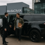 A luxury black Range Rover arrives at MediaCityUK as a professional chauffeur opens the door for a casually dressed producer with a clipboard and headphones.
