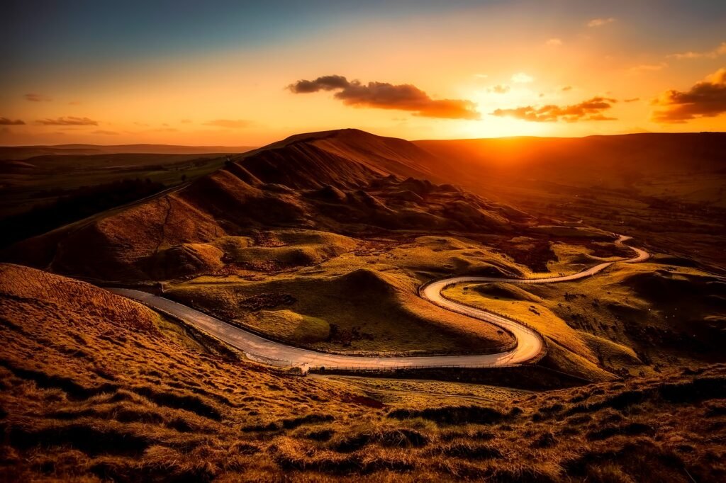 Winding mountain road through golden hills in the Peak District at sunset, known as Snake Pass – one of the most scenic driving roads in the UK. MCR EXEC

