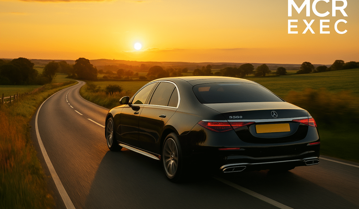 Luxury long distance chauffeur service Chester – black 2025 Mercedes S-Class driving along a winding countryside road at sunset, MCR EXEC logo in top right.