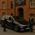 MCR EXEC chauffeur service for Manchester Marriott Victoria & Albert Hotel featuring a black 2025 Mercedes EQS. A professional chauffeur in a tailored suit opens the rear door for a business traveller carrying a briefcase, set against the hotel’s historic red-brick riverside façade.