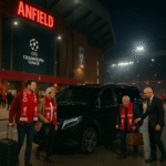 Chauffeur assists Liverpool fans in red scarves outside Anfield Stadium at night, beside a black Mercedes V-Class with MCR EXEC plate during a Champions League match.