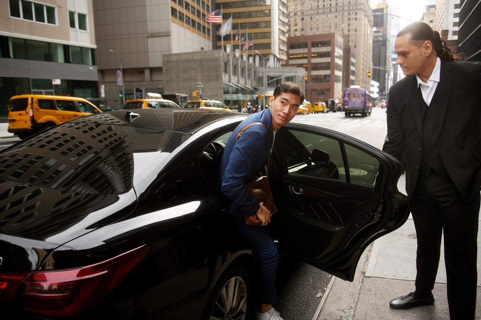 Professional chauffeur services in Manchester with a black Mercedes E-Class by MCR EXEC, chauffeur adjusting tie before client pickup outside a city hotel.