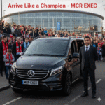 Manchester City vs Liverpool Chauffeur – Black Mercedes V-Class 2025 with MCR-EXEC number plate outside Etihad Stadium, Manchester. Professional chauffeur in tailored suit stands beside the vehicle as fans gather for the Premier League match, operated by MCR EXEC