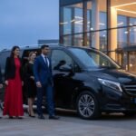Group chauffeur hire for events Manchester featuring a black Mercedes V-Class MPV with MCR-EXEC number plate, professionally chauffeured as a smartly dressed group arrives at a modern city event venue in the evening.