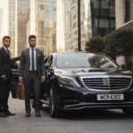 Manchester to London chauffeur price showing a black Mercedes S-Class chauffeur-driven vehicle with MCR-EXEC number plate, professional chauffeurs in business attire standing beside the car in a London financial district setting, representing premium long-distance executive travel.