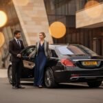 Multi day chauffeur hire for events using a black Mercedes S-Class with MCR-EXEC number plate, professional chauffeur assisting an elegantly dressed event guest outside a modern city venue