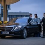 VIP event transport Manchester featuring a black Mercedes-Benz S-Class with MCR-EXEC number plate as a professional chauffeur assists VIP guests outside a modern event venue during evening arrival.