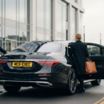 Corporate travel duty of care executive chauffeur service by MCR EXEC, showing a professional chauffeur assisting a business traveller beside a black Mercedes saloon outside a modern office building in the UK