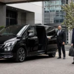 How to choose a corporate chauffeur company UK guide showing a latest 2025 black Mercedes V-Class with MCR EXEC number plate outside a Manchester business hotel, with a professional chauffeur assisting an executive passenger.