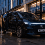 Mercedes VLE EV chauffeur industry news image showing a black Mercedes executive MPV with MCR EXEC number plate outside a modern Manchester business hotel at dusk, with a professional chauffeur assisting a corporate passenger, representing the future of electric luxury MPV chauffeur travel in the UK.