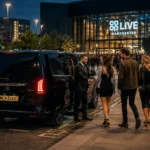 Black Mercedes V-Class with MCR EXEC number plate arriving for a Kings of Leon Co-op Live chauffeur booking in Manchester, with a professional chauffeur opening the rear door for concert guests.