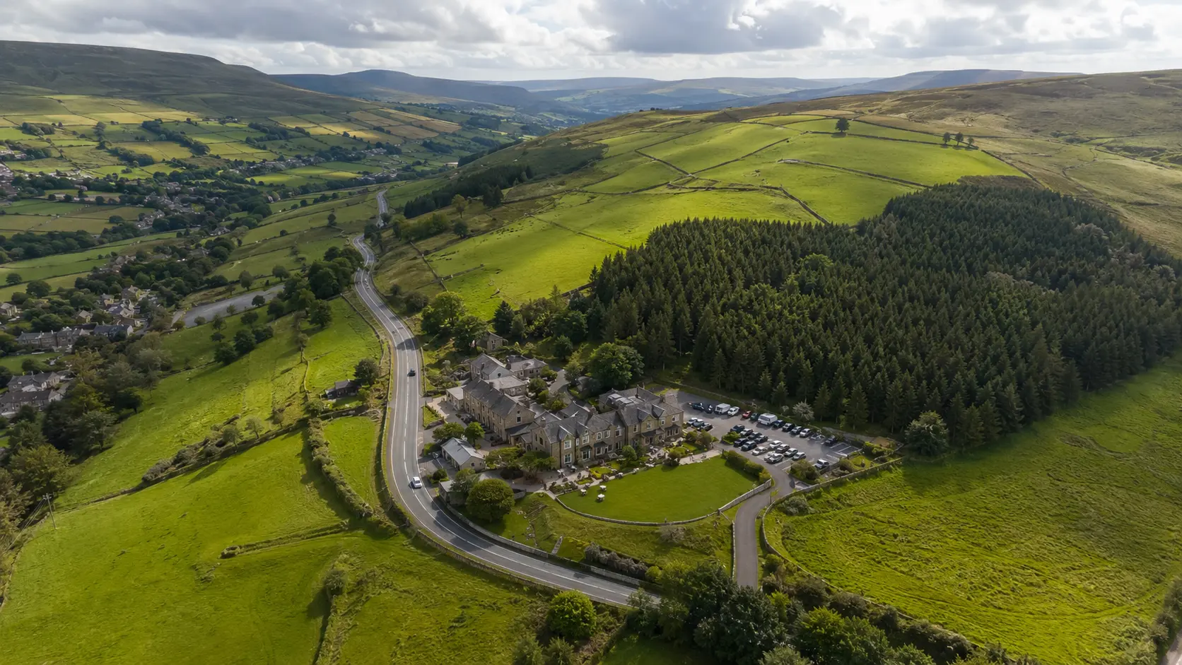 Vue aérienne des collines verdoyantes de Saddleworth, de ses champs de pierres sèches, de ses bois et d'un hôtel de campagne au bord d'une route sinueuse.