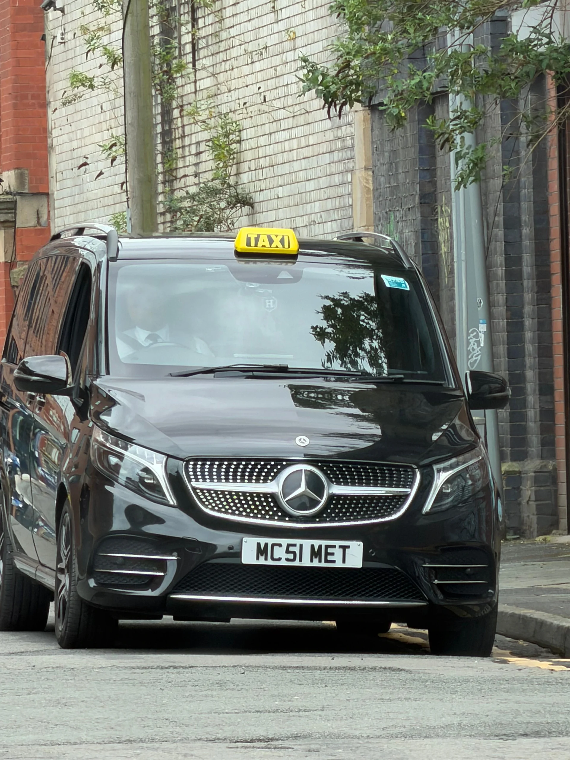 Black Mercedes V-Class with a yellow taxi roof sign fitted for the Booking.com advert
